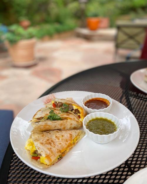 A plate with two quesadillas filled with eggs and vegetables, served with green and red sauces on the side.