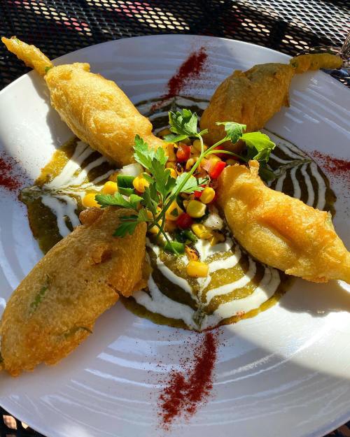 A plate of golden fried snacks arranged around a colorful sauce, garnished with herbs and vegetables.