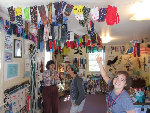 A colorful display of socks hangs from the ceiling in a cozy shop, with three people chatting and smiling.