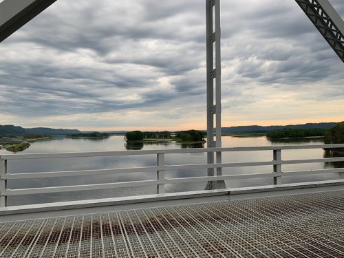 A view from a bridge overlooking a calm river with islands and a cloudy sky at sunset.