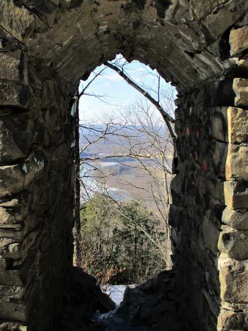 View through a stone archway, showcasing a scenic landscape with trees and a river in the distance.