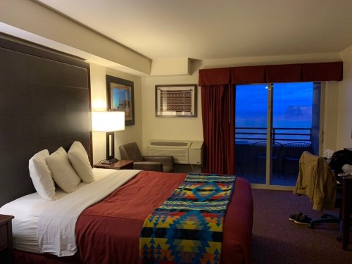A cozy hotel room with a king bed, colorful blanket, and a view of the ocean through a large window.