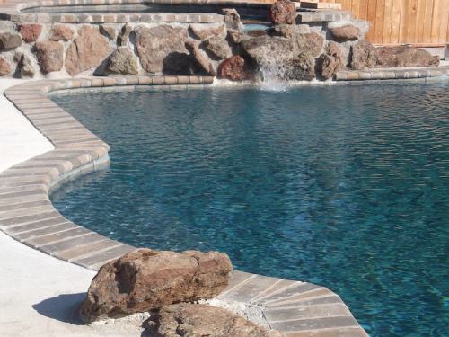 A serene swimming pool with a stone border and a small waterfall, surrounded by natural rock formations.
