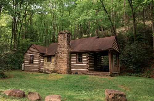 A rustic log cabin with a stone chimney, surrounded by lush green trees and grass.