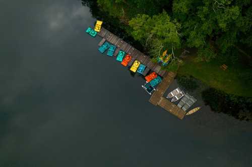 Aerial view of a dock with colorful boats on a calm lake surrounded by lush greenery.