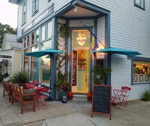 A cozy café with outdoor seating, colorful umbrellas, and a welcoming entrance, featuring a chalkboard menu.