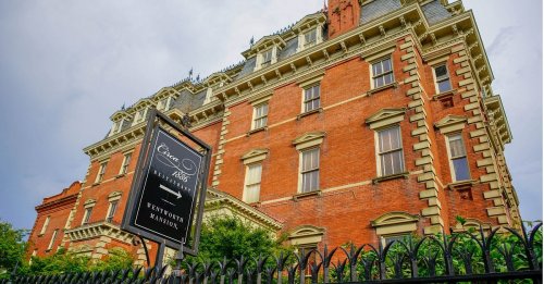 Historic red brick building with ornate architecture, featuring a sign for "Cedar Hill" and a wrought iron fence.