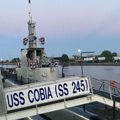 The USS Cobia (SS 245) submarine docked, with a full moon rising in the background and festive decorations.