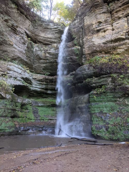 A serene waterfall cascading down a rocky cliff, surrounded by lush greenery and a small pool at the base.