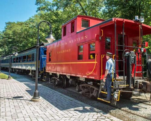 A red caboose and blue train cars at a railroad station, with a conductor standing beside the caboose.