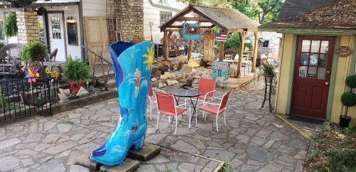 A colorful oversized boot sculpture in a quaint outdoor space with a patio, tables, and a wooden gazebo.