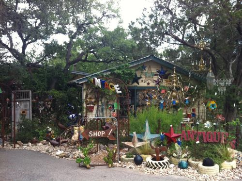 A colorful vintage shop surrounded by eclectic decorations and greenery, featuring signs and various artistic items.