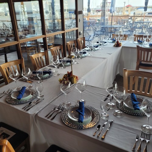 A beautifully set dining table with elegant tableware and blue napkins, overlooking a waterfront view.