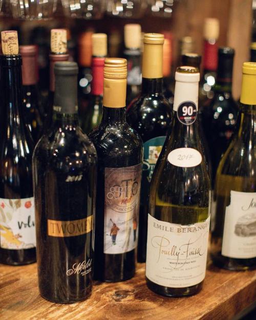A selection of wine bottles on a wooden shelf, featuring various labels and colors.