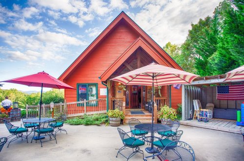 A charming orange cabin with a porch, surrounded by outdoor seating and umbrellas, set against a blue sky.