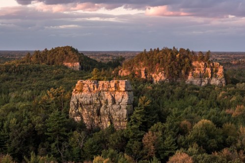 Scenic view of rocky outcrops surrounded by lush green trees under a colorful sunset sky.
