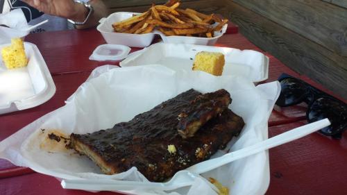 A plate with two ribs, cornbread, and sweet potato fries on a red table.