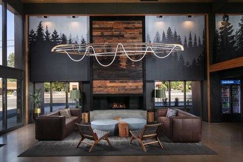 Modern lobby with a circular seating area, wooden accents, a large light fixture, and forest-themed wall art.