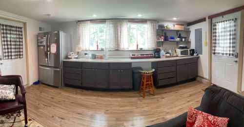 A cozy kitchen with wooden floors, a large window, and modern appliances, featuring a mix of dark cabinets and light decor.