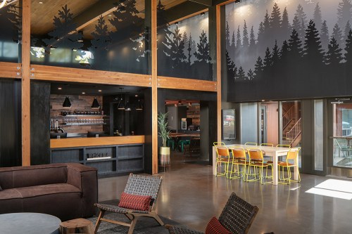 Modern interior of a cozy café with wooden accents, large windows, and forest-themed wall art.