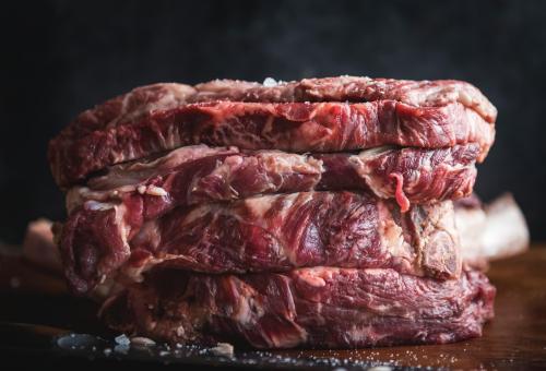 A close-up of stacked raw beef cuts with visible marbling and a sprinkle of salt on top, set against a dark background.
