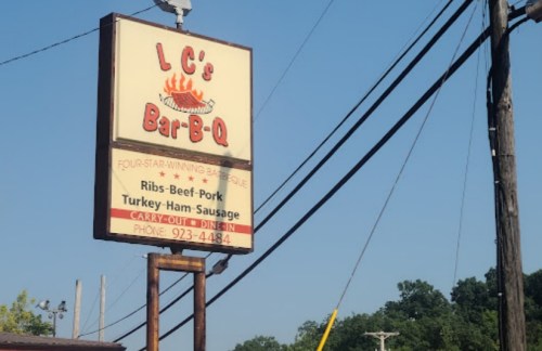 Sign for LC's Bar-B-Q featuring menu items like ribs, beef, pork, turkey, and ham sausage against a clear blue sky.
