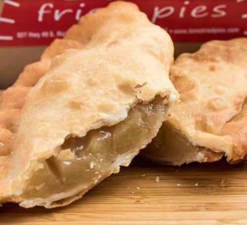 Two golden-brown fried pies, one cut open to reveal a sweet filling, resting on a wooden surface.