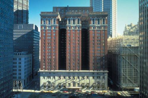 Historic brick building with ornate architecture, flanked by modern skyscrapers and construction, in a city setting.