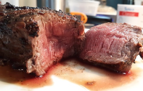 Juicy, medium-rare steak with a seared crust, sliced to reveal its tender pink interior on a white plate.