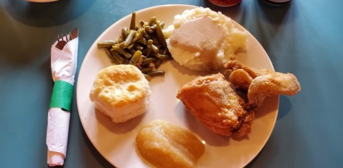 A plate of fried chicken, mashed potatoes with gravy, green beans, a biscuit, and applesauce.
