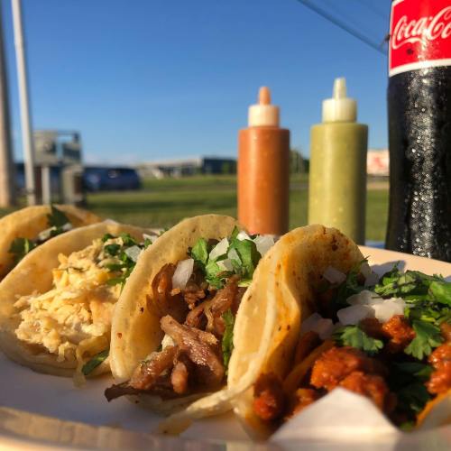 A plate of tacos filled with various meats, topped with cilantro and onions, with sauces and a Coke in the background.