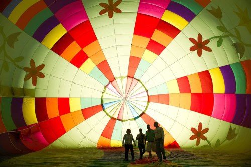 Four people stand inside a colorful hot air balloon, surrounded by vibrant patterns and light.