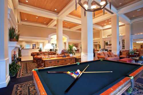 A spacious lounge with a pool table in the foreground, elegant furniture, and warm lighting in a welcoming atmosphere.