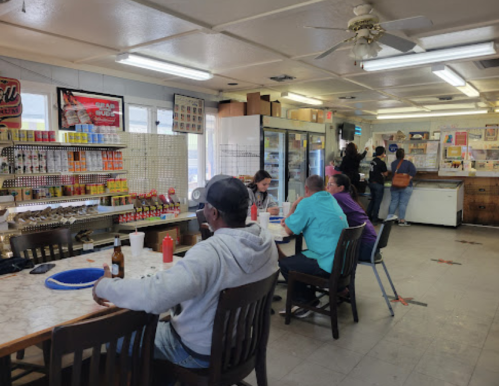 A casual diner interior with patrons at tables, condiments on the counter, and a variety of food items displayed.