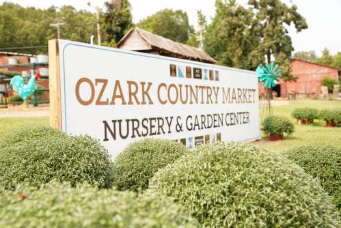 Sign for Ozark Country Market Nursery & Garden Center, surrounded by green shrubs and trees in the background.