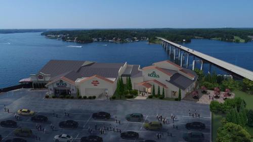 Aerial view of a lakeside building complex with a parking lot, bridge, and water in the background.