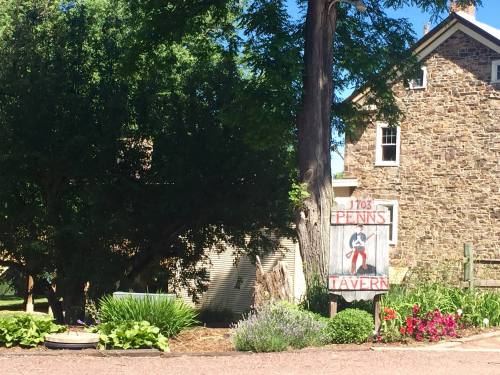 A rustic sign for Penn's Tavern stands in front of a stone building, surrounded by greenery and colorful flowers.