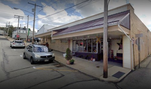A small storefront with a "OPEN" sign, parked cars nearby, and power lines overhead on a cloudy day.