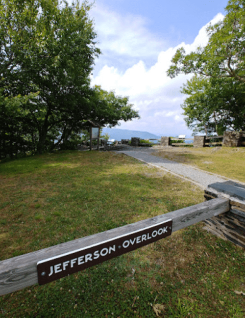 Sign for "Jefferson Overlook" in a grassy area with trees and a cloudy sky in the background.