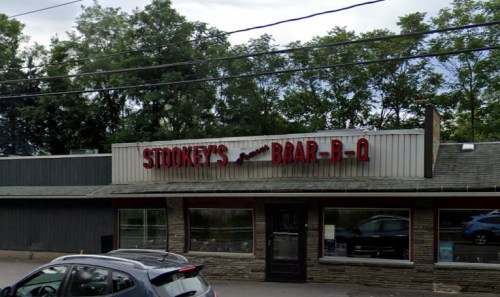 Exterior of Stookey's Bar-B-Q restaurant with a sign and large windows, surrounded by trees and a cloudy sky.