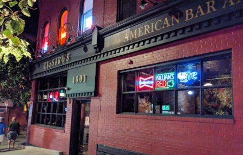 Exterior of a bar with neon signs, featuring "Budweiser," "Killian's Red," and "Miller Lite," on a brick building.