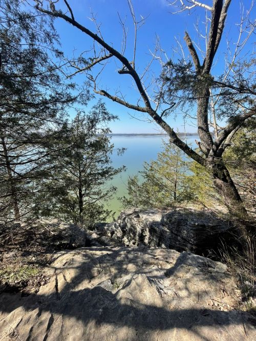 A rocky overlook with trees framing a serene lake under a clear blue sky.