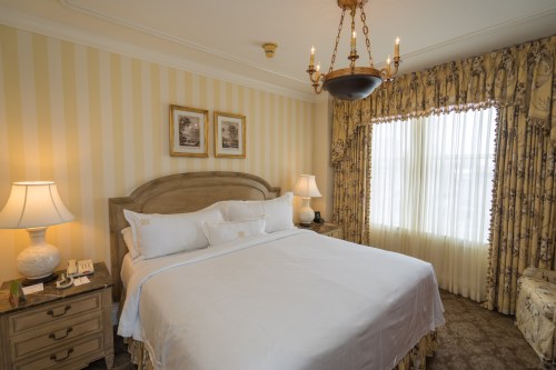 A cozy hotel room featuring a large bed, elegant decor, and soft lighting from lamps and a chandelier.