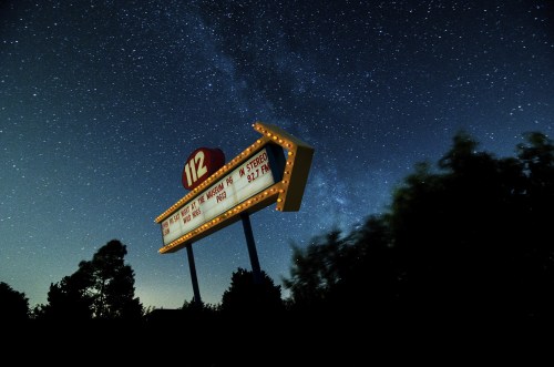 A vintage marquee sign illuminated against a starry night sky, surrounded by silhouettes of trees.
