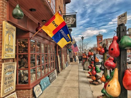 A vibrant street scene with shops, colorful flags, and decorative gourds lining the sidewalk under a blue sky.