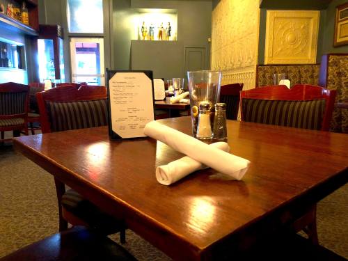 A restaurant table set with a menu, rolled napkins, and condiments, in a cozy dining area.