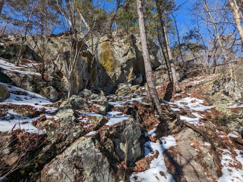 Rocky terrain with scattered snow and trees under a clear blue sky.