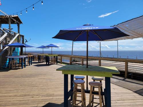 Outdoor deck with colorful tables and umbrellas overlooking the ocean under a clear blue sky.