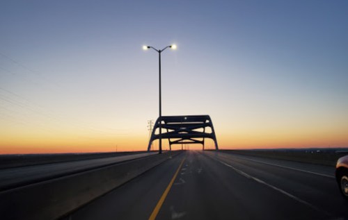 A view of a bridge at sunset, with streetlights illuminating the road and a gradient sky in the background.