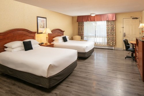 A hotel room with two queen beds, a desk, and a window with curtains, featuring warm colors and wooden furniture.